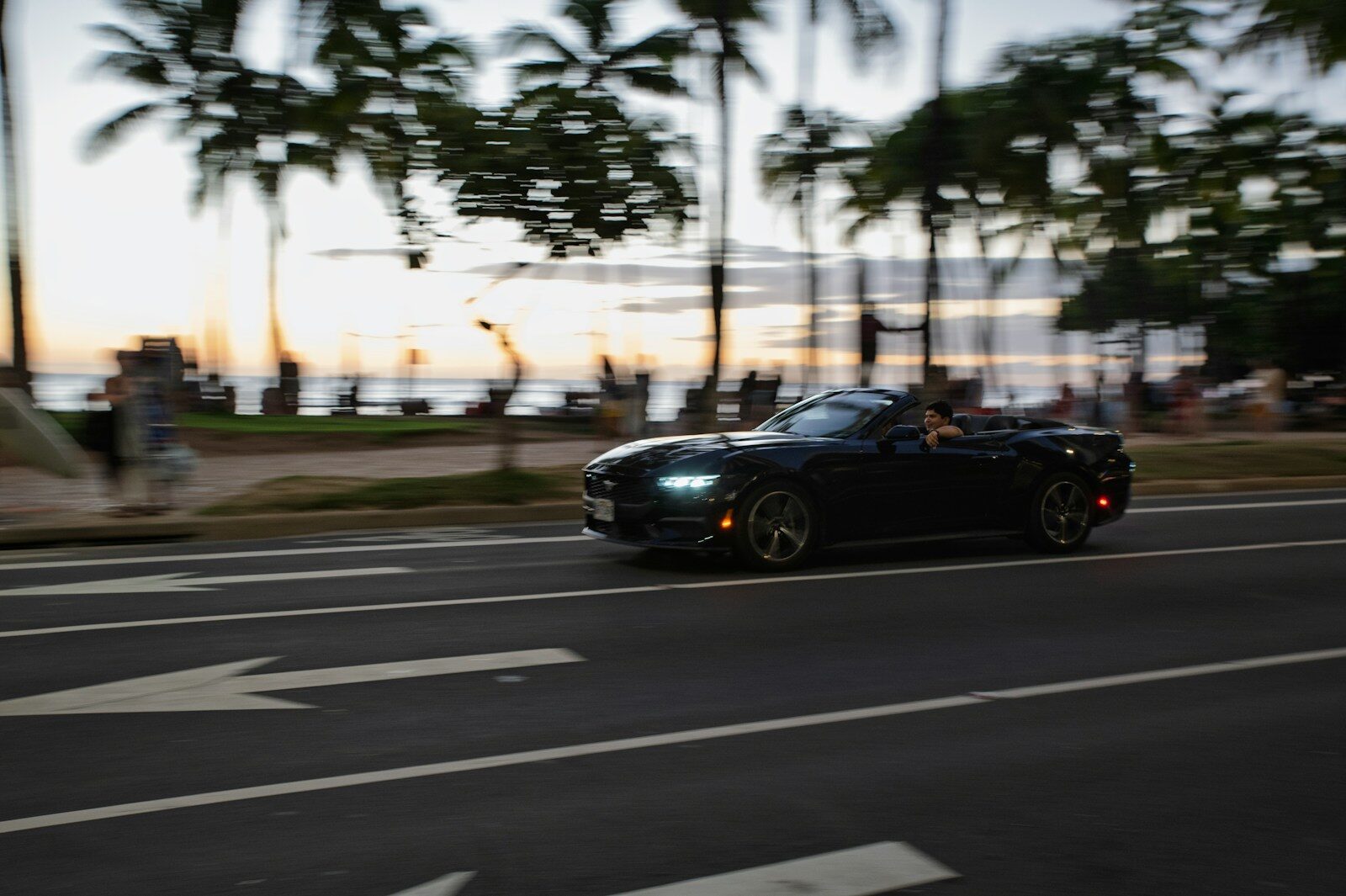 Black convertible driving on a coastal road at dusk